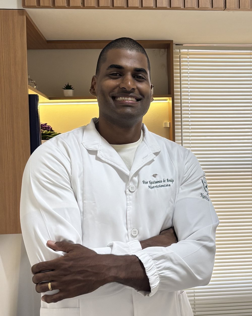 Vitor Nascimento, nutricionista esportivo, de jaleco e braços cruzados no consultório